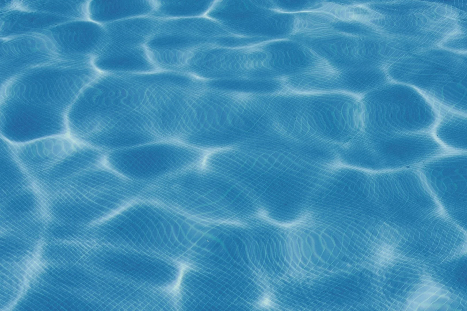 Sunlight reflecting on rippling clear blue swimming pool water